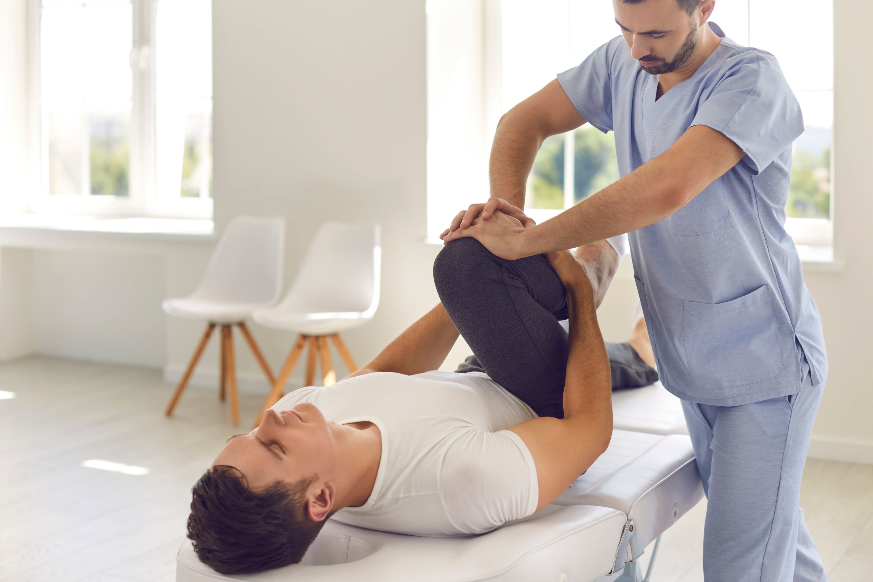 Physical therapist assisting a client on a treatment table during leg rehabilitation